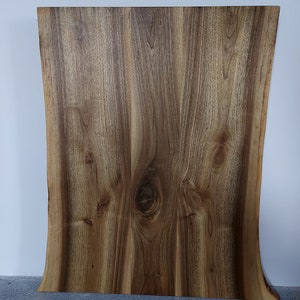 May include: A large, natural wood slab with a live edge and a unique grain pattern. The wood is a rich brown color with streaks of lighter wood. The slab has a natural curve along the bottom edge.