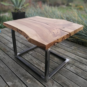 May include: A wooden coffee table with a live edge top and a black metal frame. The table is sitting on a wooden deck.