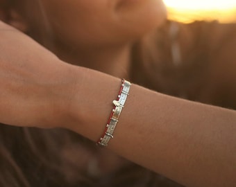 May include: A woman's hand wearing several silver rings, including a large, ornate ring with a detailed design. The hand is resting on her other arm, and she is wearing a silver bracelet on her wrist.