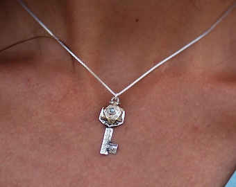 May include: A silver chain necklace with a key pendant. The key is made of silver and gold and has a star of David design on the top. The star of David is surrounded by a circle of small stones.