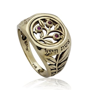 May include: A gold ring with a circular design featuring a pomegranate branch with three red gemstones. The ring has Hebrew text and leaf patterns. The ring is made of 9K gold.