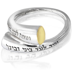 May include: A silver ring with a gold band and Hebrew writing. The writing says "Blessed are you, Lord our God, King of the Universe, who sanctifies us with His commandments and commands us to engage in the study of Torah."
