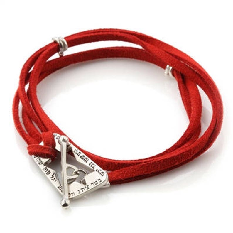 May include: Red suede wrap bracelet with a silver-tone clasp. The bracelet features a triangular clasp with engraved text. The wrap design allows for multiple turns around the wrist. The bracelet is a vibrant accessory.