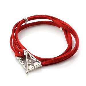 May include: Red suede wrap bracelet with a silver-tone clasp. The bracelet features multiple strands of red suede and a triangular clasp with engraved text. The clasp has a bar closure.