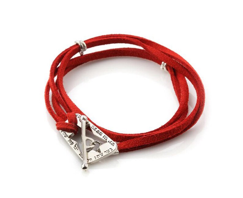 May include: Red suede wrap bracelet with a silver-tone clasp. The bracelet features multiple strands of red suede and a triangular clasp with engraved text. The clasp has a bar closure.