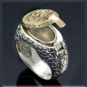 May include: A silver ring with a hinged top that opens to reveal a small compartment. The top of the ring is decorated with a gold Star of David and Hebrew lettering. The band of the ring has a textured, scaly design.