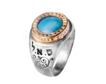Op de afbeelding: Zilveren ring met een goudkleurige bezel en een turkoois steen. De ring heeft gegraveerde Hebreeuwse letters en decoratieve krullen op de band. De turkoois steen is ovaal van vorm en gezet in een goudkleurige bezel.