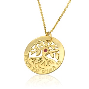 May include: Gold necklace with a round pendant featuring a tree of life design with a red gemstone in the center. The pendant is engraved with Hebrew text.