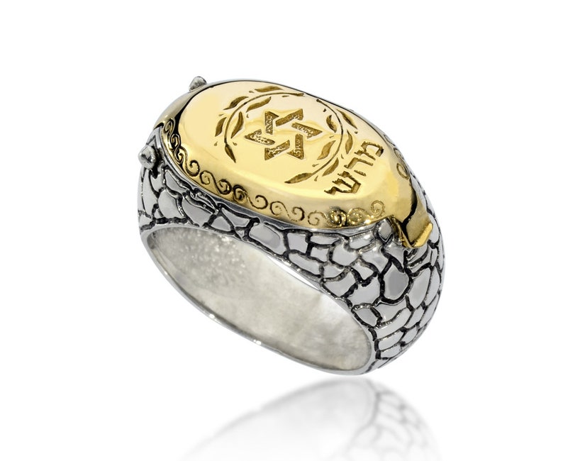 May include: A silver ring with a textured band and a gold oval top. The top features a Star of David and the Hebrew word "שלום" (peace) in gold.