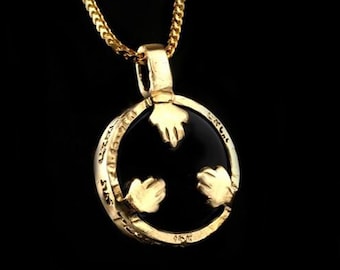May include: A gold pendant necklace featuring a black circular centre with three leaf-like shapes. The pendant has engraved text around the edge and is suspended from a gold chain. The background is black.