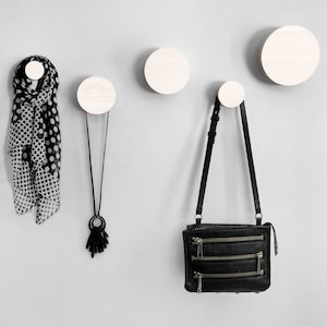May include: Three white wooden wall hooks with a black polka dot scarf, a black necklace with a pendant, and a black leather purse hanging from them.