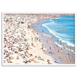 May include: A photograph of a crowded beach with people sunbathing, swimming, and walking along the shore. The water is blue and the sand is white. The beach is surrounded by a white frame.