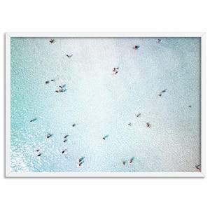 May include: An aerial view of a turquoise blue body of water with many people swimming and wading in the shallows. The water is clear and the sand is white.