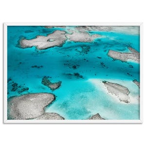 May include: An aerial view of a turquoise ocean with white coral reefs. The water is clear and shallow, revealing the coral formations below.