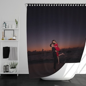 May include: A couple in love, embracing on a beach at sunset. The woman is wearing a red dress and the man is wearing a black shirt. The couple is silhouetted against the orange and purple sky.