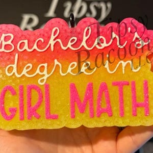 May include: A colorful, cloud-shaped charm with the words "Bachelor degree GIRL MATH" in white and pink lettering. The charm has a gradient of pink, orange, and yellow. A small black loop is at the top.
