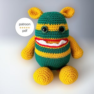 May include: A green and yellow striped crocheted monster toy with a big red mouth and white teeth. The monster has large yellow ears and big green eyes.