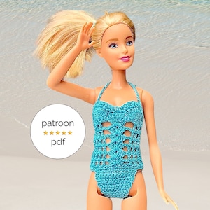 Op de afbeelding: Een blauwe gehaakte badpak voor een pop. Het badpak heeft een haltertop en een hoog uitgesneden been. De pop draagt ​​het badpak en heeft blond haar. De achtergrond is een wit zandstrand met blauw water.