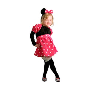 Op de afbeelding: Een jong meisje verkleed als Minnie Mouse. Ze draagt een zwart-wit geblokt jurkje met een zwarte strik op haar hoofd.
