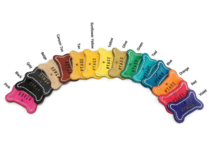 May include: A collection of colorful leather pet tags in various shades, including pink, black, grey, beige, tan, yellow, green, blue, orange, red, and violet. Each tag is stitched with white thread and features the word "PTAGS".