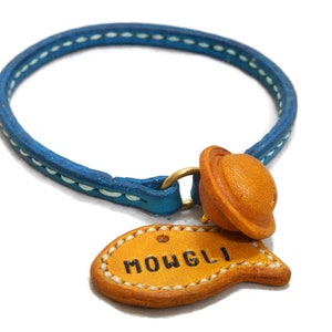 May include: A blue leather dog collar with white stitching and a brown leather tag that says "MOWGLI".