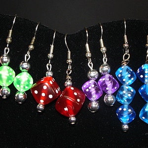 May include: A set of 8 pairs of dangle earrings featuring dice charms in various colors, including pink, green, red, purple, blue, and orange. Each charm is a clear plastic dice with white dots.