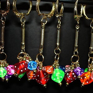 May include: Six gold keychains with colorful dice charms. The dice are translucent and have different colors, including red, green, blue, and yellow.