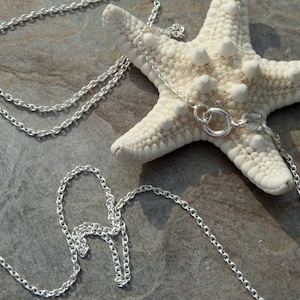 May include: A silver chain necklace with a lobster clasp. The chain is lying on a gray stone surface with a white starfish.