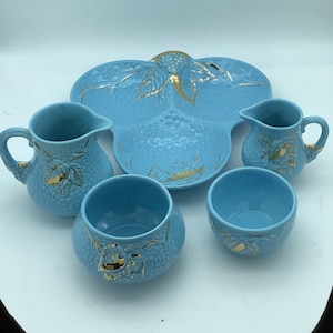 Op de afbeelding: Een blauwe en gouden keramische serveerset met een grote, driedelige serveerschaal en twee roomkannen en twee suikerpotten. De set heeft een druivenrankenontwerp met gouden accenten.