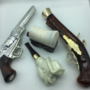 May include: A set of four vintage glass perfume bottles shaped like a cowboy hat, a covered wagon, a pistol, and a revolver. The bottles are made of clear glass with a white porcelain finish. The bottles are decorated with gold accents.