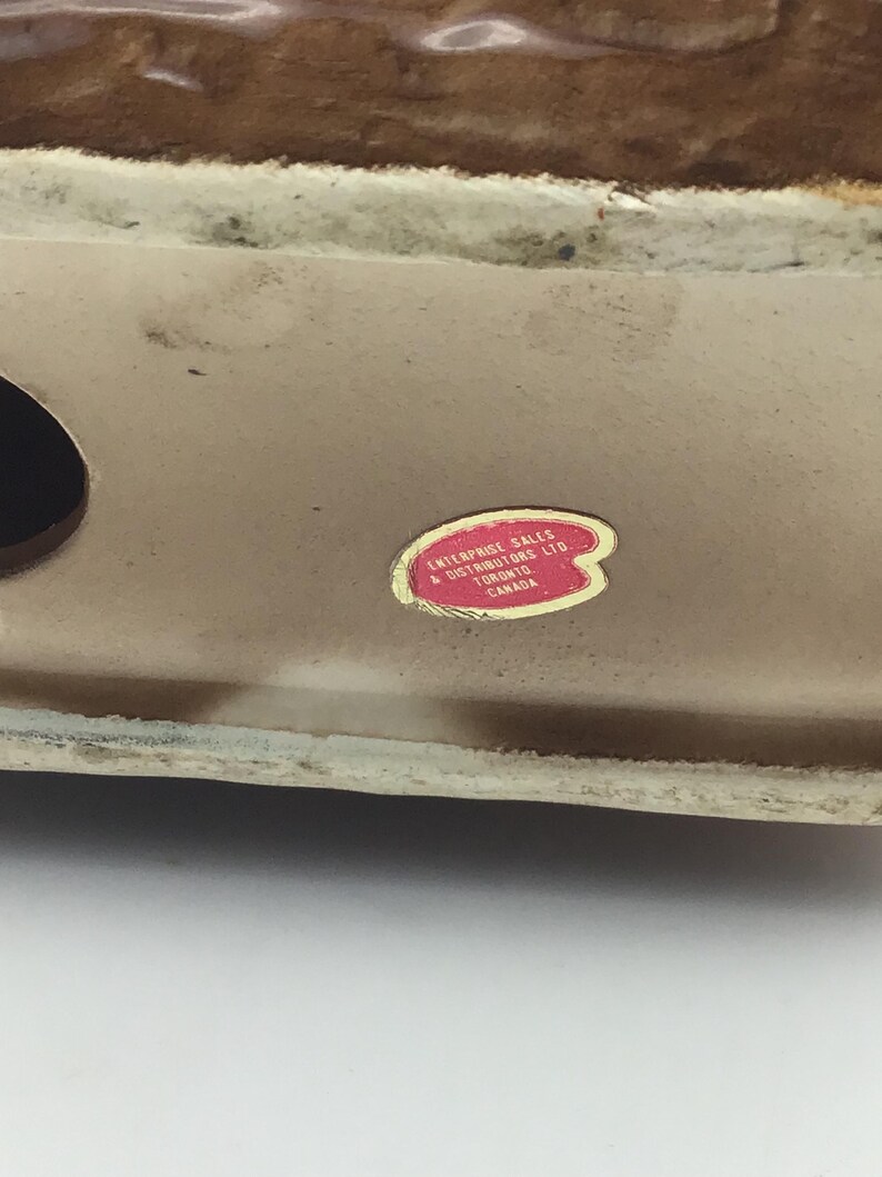 May include: Close-up of a brown ceramic figurine with a red sticker that reads "Enterprise Sales & Distributors Ltd. Toronto Canada."