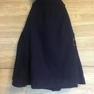 Op de afbeelding: Een marineblauwe rok met een geplooid ontwerp. De rok wordt getoond op een mannequin en heeft een zoom tot op de knie. De stof lijkt een materiaal van gemiddeld gewicht te zijn, geschikt voor verschillende seizoenen. De rok heeft een klassieke, tijdloze stijl.