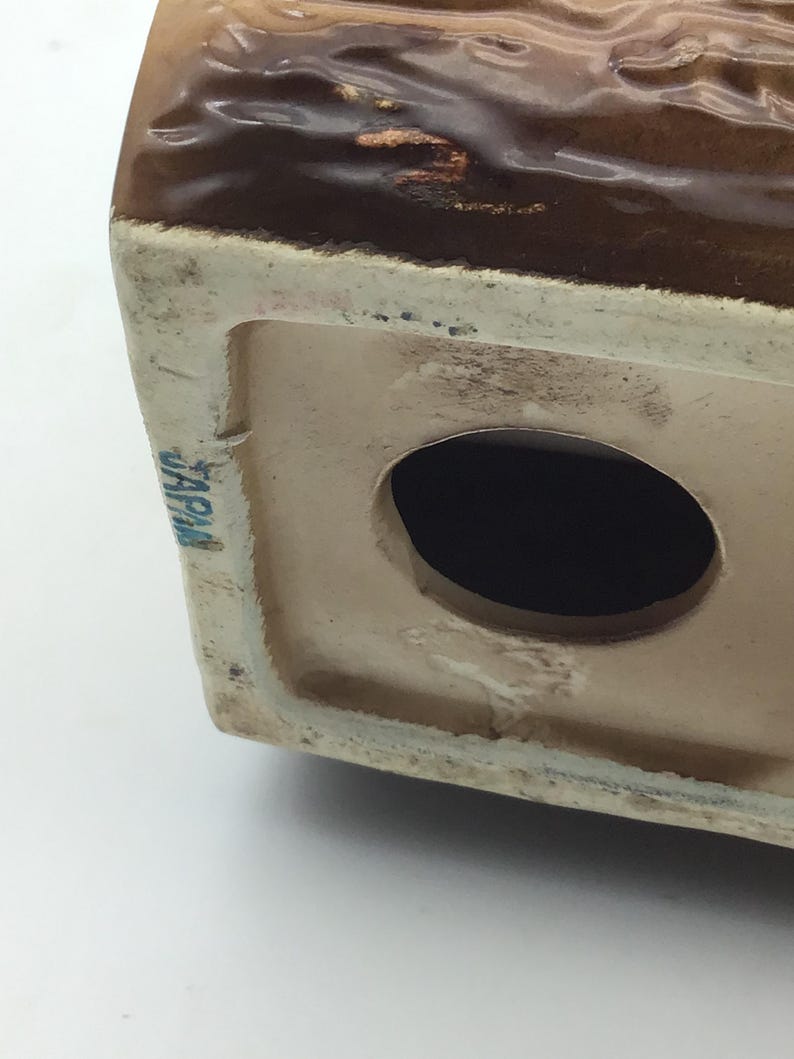 May include: A brown ceramic figurine with a hole in the bottom. The figurine has a brown glaze and the words "JAPAN" are printed on the bottom.
