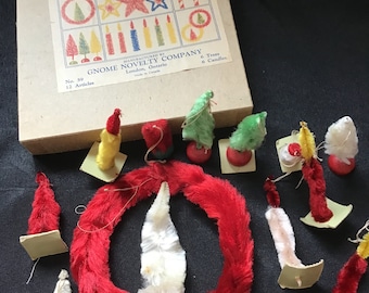 May include: A vintage box of 12 Christmas tree ornaments, including 6 trees and 6 candles. The box is labeled "Gnome Novelty Company" and "No. 59". The ornaments are made of white, green, and yellow felt and have a red base.