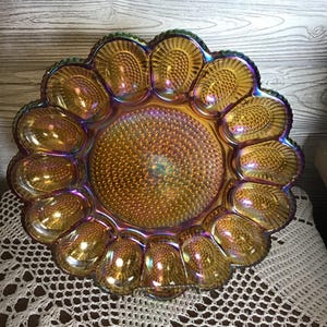 May include: Iridescent amber glass serving dish with a sunflower design. The dish features a central, textured circle surrounded by petal-shaped compartments. The glass has a shimmering, multi-colored finish.