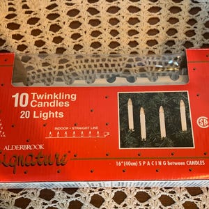May include: A red rectangular box for Alderbrook Signature 10 Twinkling Candles and 20 Lights. The packaging features white text, a graphic of four lit candles on pine branches, and specifies 40cm spacing between the candles.