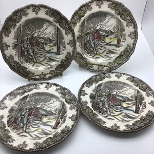 Könnte beinhalten: Set aus vier braunen und grünen Keramik-Dinnertellern mit einer Winterszene mit einem roten Schuppen, Bäumen und Schnee. Die Teller haben einen gewellten Rand.