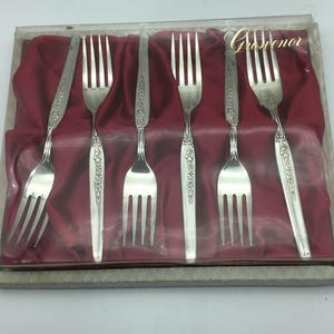 Puede incluir: Un juego de seis tenedores de plata en una caja forrada de terciopelo rojo. La caja está etiquetada con "Grosvenor".