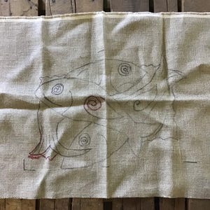 May include: A beige canvas with a black and red embroidery design of three fish. The fish are outlined in black and have red details.
