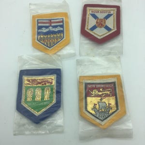 Peut inclure: Quatre écussons en tissu vintage, chacun dans une pochette en plastique transparent. Les écussons présentent des armoiries provinciales et du texte, dont "NOVA SCOTIA", "SASKATCHWAN" et "NEW BRUNSWICK". Les écussons ont des accents dorés, bleus, rouges et jaunes.