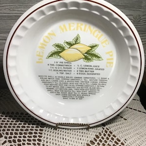 May include: White ceramic pie dish with a brown rim and a decorative edge. The dish features the words "Lemon Meringue Pie" and a lemon graphic. Recipe instructions are printed on the dish.