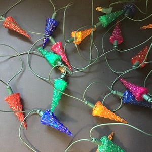 Pode incluir: Uma sequência de luzes de Natal coloridas com lâmpadas em forma de cone em várias cores, incluindo vermelho, azul, verde, laranja e rosa. As luzes são conectadas por um fio verde, em um fundo escuro.