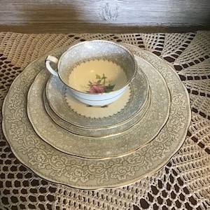 以下が含まれることがあります： ティーカップ、ソーサー、2枚のプレートを備えたヴィンテージティーセット。 セットは、ティーカップにピンクのバラが付いた、明るいグレーとゴールドの花柄です。 プレートとティーカップの縁は金色のトリムです。