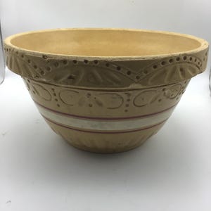 May include: A large, yellow ceramic mixing bowl with a white and red stripe around the middle. The bowl has a decorative design around the top edge.