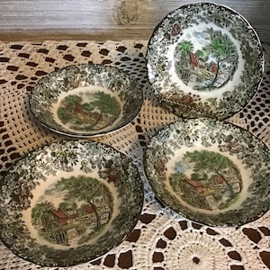 May include: Four vintage ceramic bowls. Each bowl has a central landscape scene with a red building, trees, and water. The rims have a detailed black and white floral pattern with a gold trim. The bowls are on a white lace doily.
