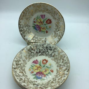 May include: Set of four white ceramic bowls with a gold floral pattern and a colourful embroidered floral design in the centre.