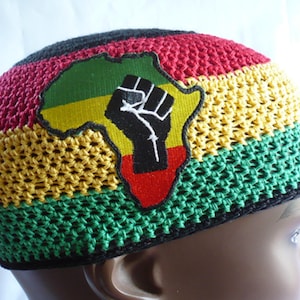 May include: A crocheted beanie in the colors of the Pan-African flag: red, yellow, and green. The hat features an embroidered patch of the African continent with a raised black fist, symbolizing solidarity and resistance.