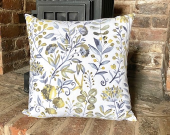 May include: A white cushion with a floral pattern in shades of grey and yellow. The cushion is sitting on a brick surface.