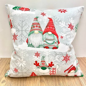 May include: A grey throw pillow with a Christmas gnome pattern. The gnomes are wearing red and green hats and have white beards. The background is a grey and white snowflake pattern.