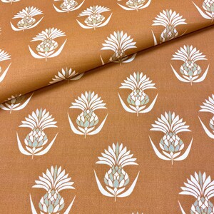 Può includere: Un tessuto marrone con un motivo ripetuto di ananas stilizzati bianchi. Gli ananas hanno un centro blu chiaro e verde.